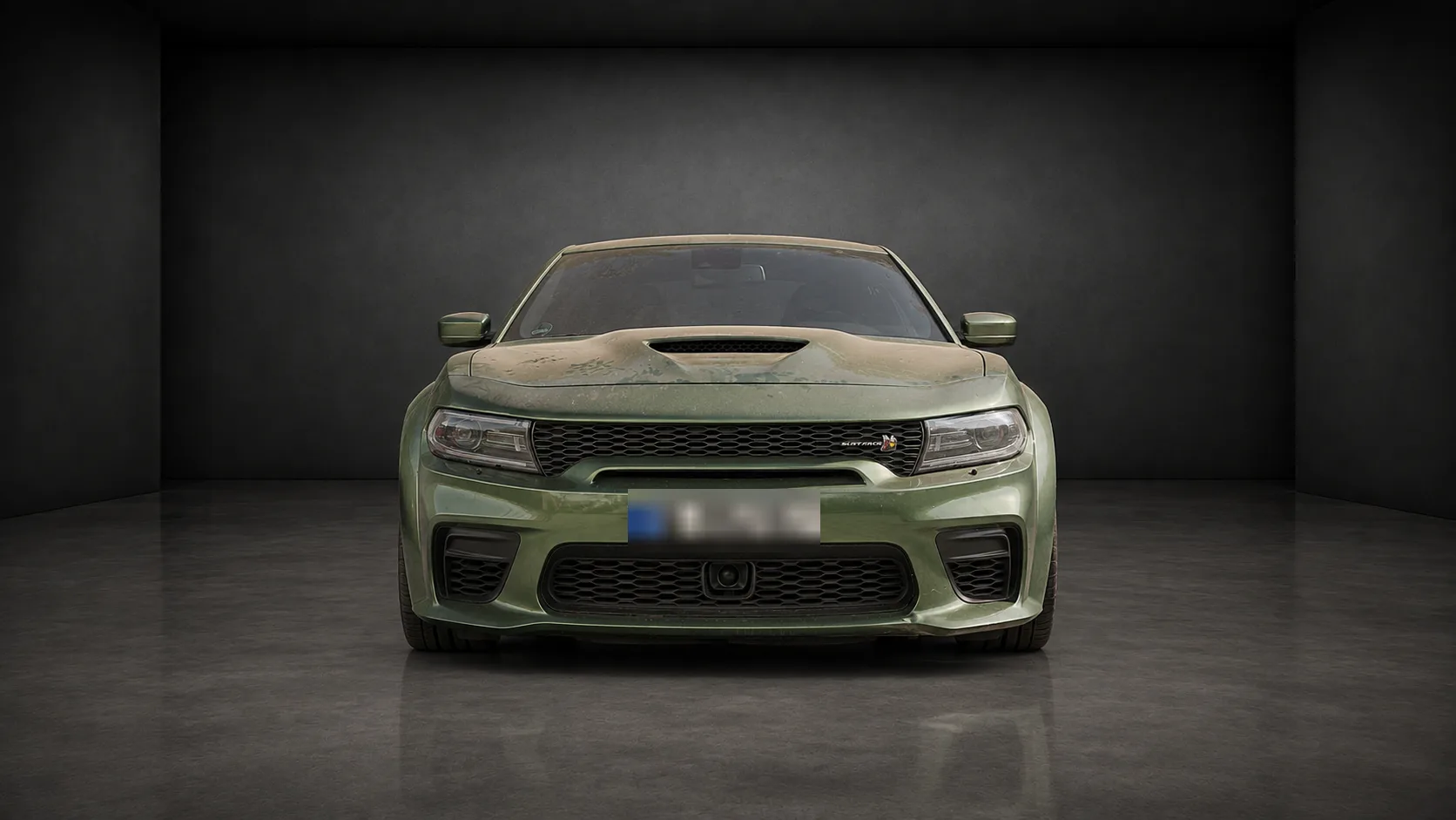 Dodge Charger Widebody in mattem Militärgrün, frontal von vorn, in einer dunklen Halle
